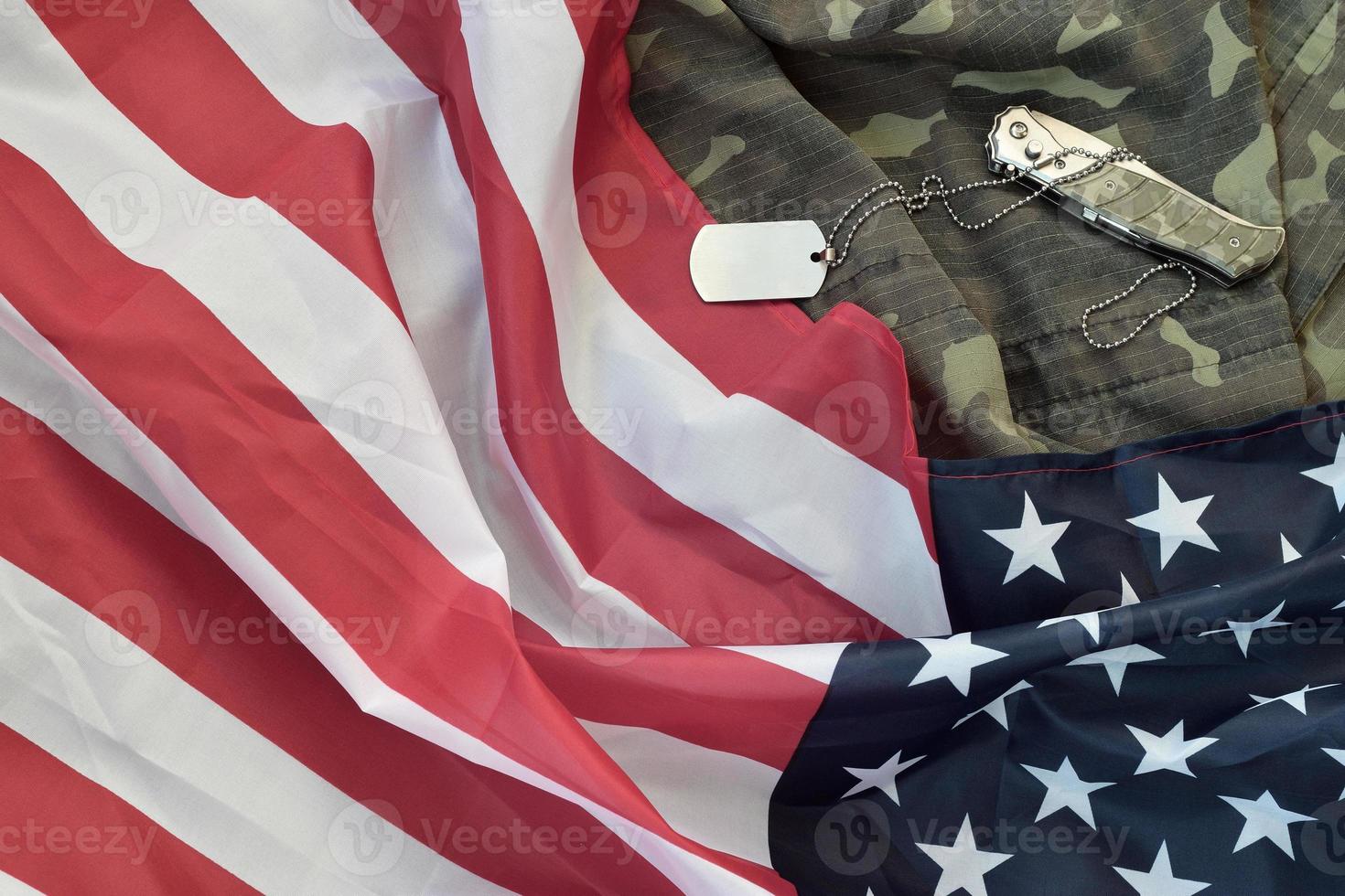 Army dog tag token and knife lies on Old Camouflage uniform and folded United States Flag photo