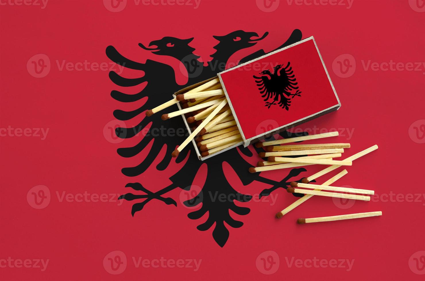 Albania flag  is shown on an open matchbox, from which several matches fall and lies on a large flag photo