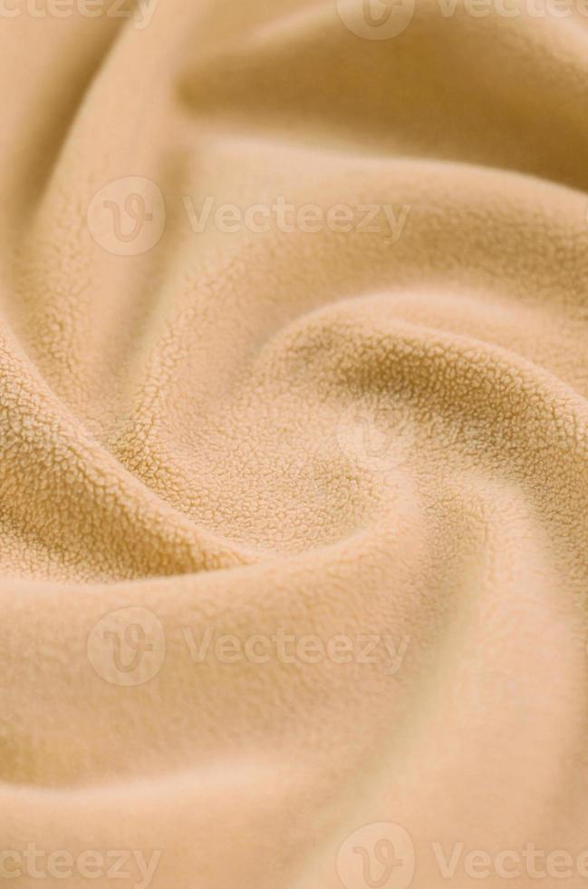The blanket of furry orange fleece fabric. A background of light orange soft plush fleece material with a lot of relief folds photo