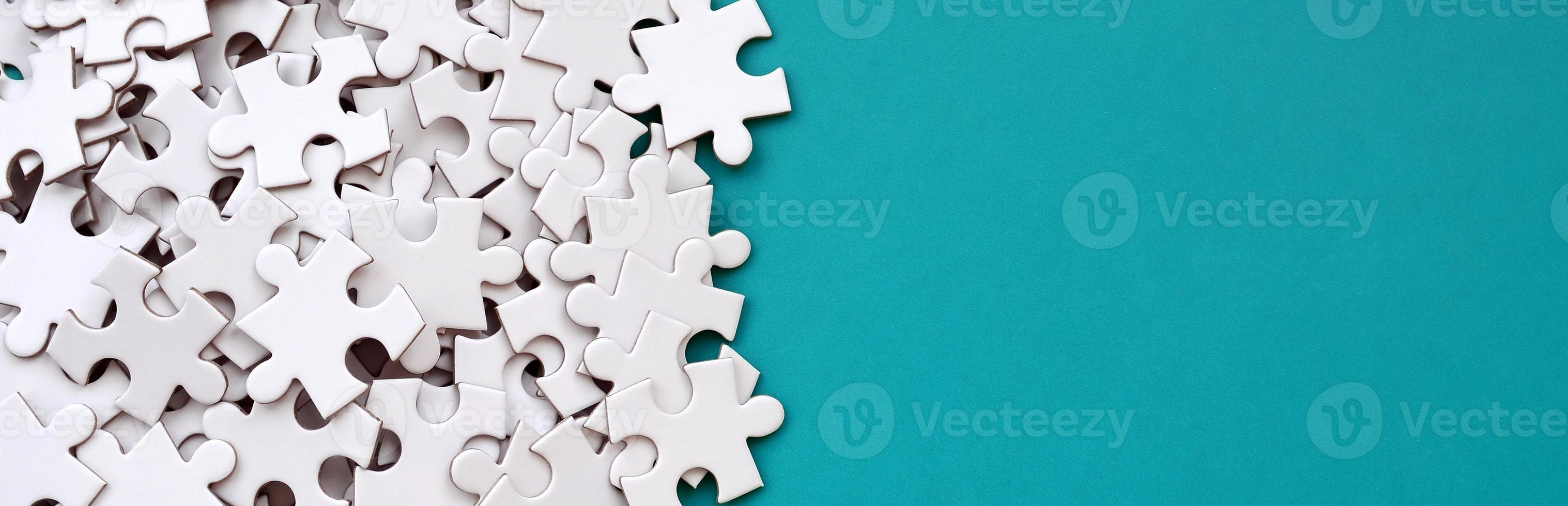 A pile of uncombed elements of a white jigsaw puzzle lies on the background of a blue surface. Texture photo with copy space for text