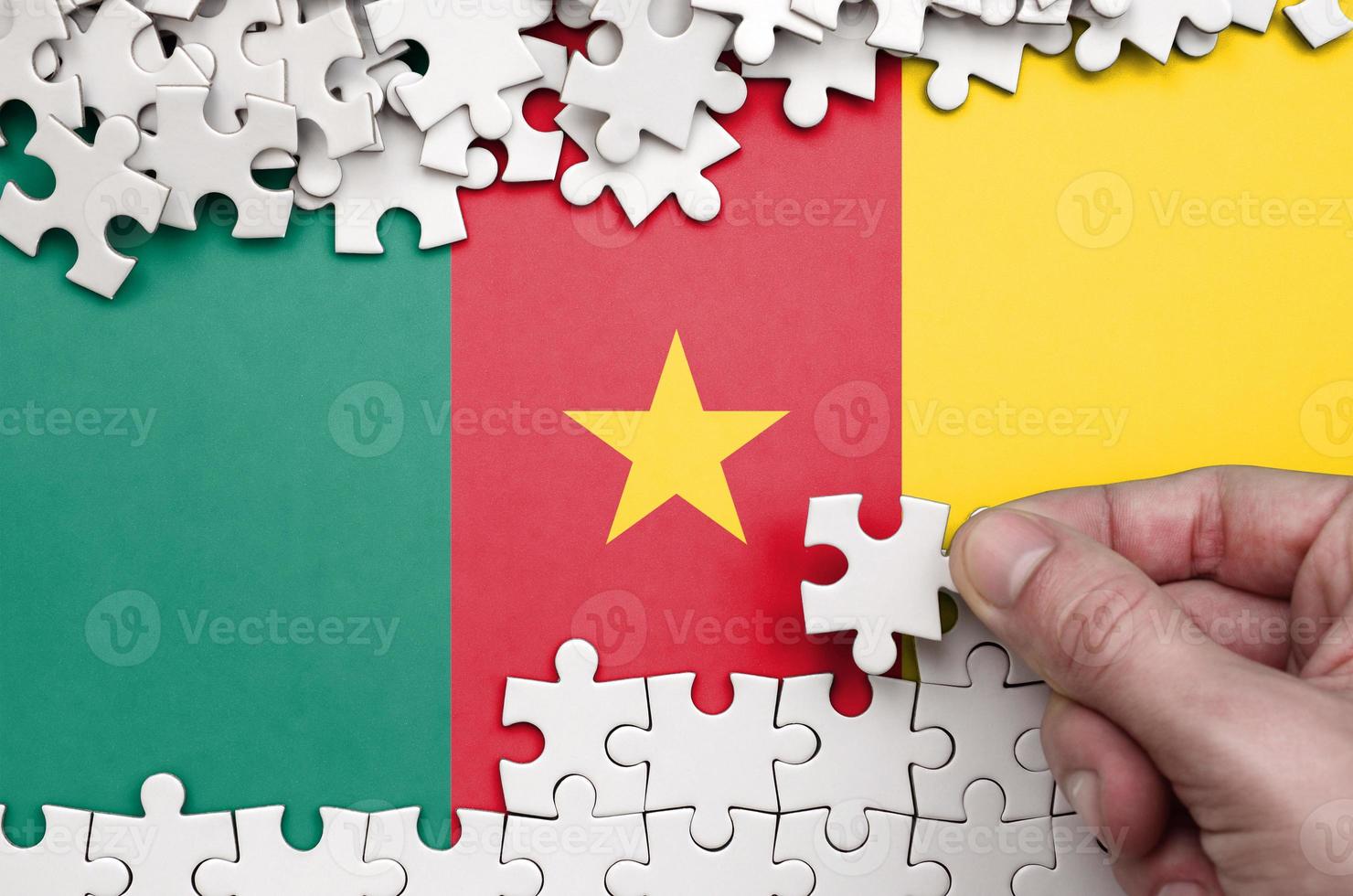 Cameroon flag  is depicted on a table on which the human hand folds a puzzle of white color photo