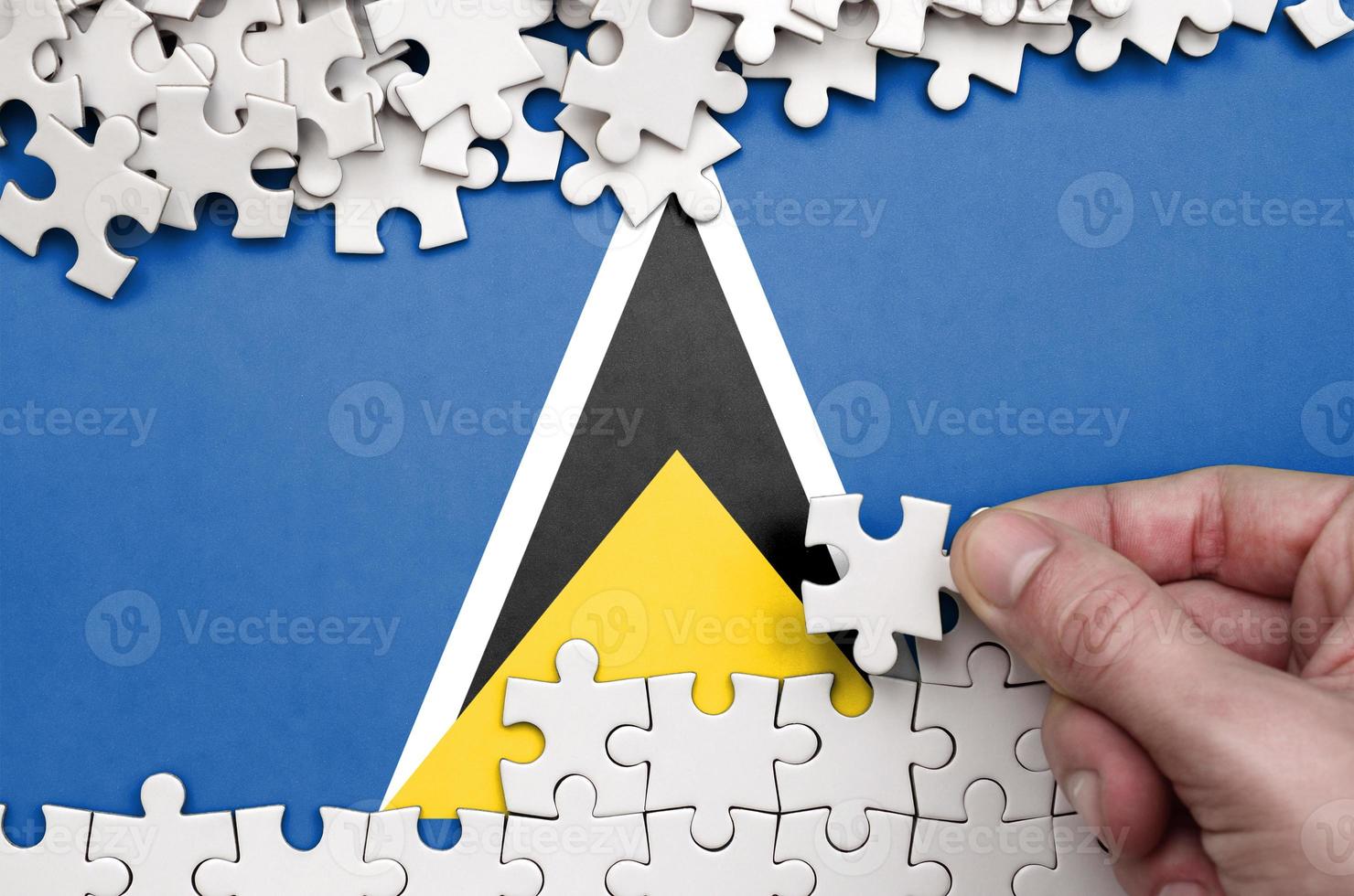 Saint Lucia flag  is depicted on a table on which the human hand folds a puzzle of white color photo
