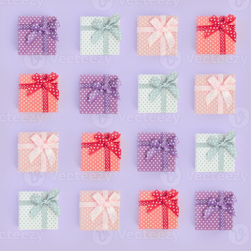 Piles of a small colored gift boxes with ribbons lies on a violet background. Minimalism flat lay top view pattern photo