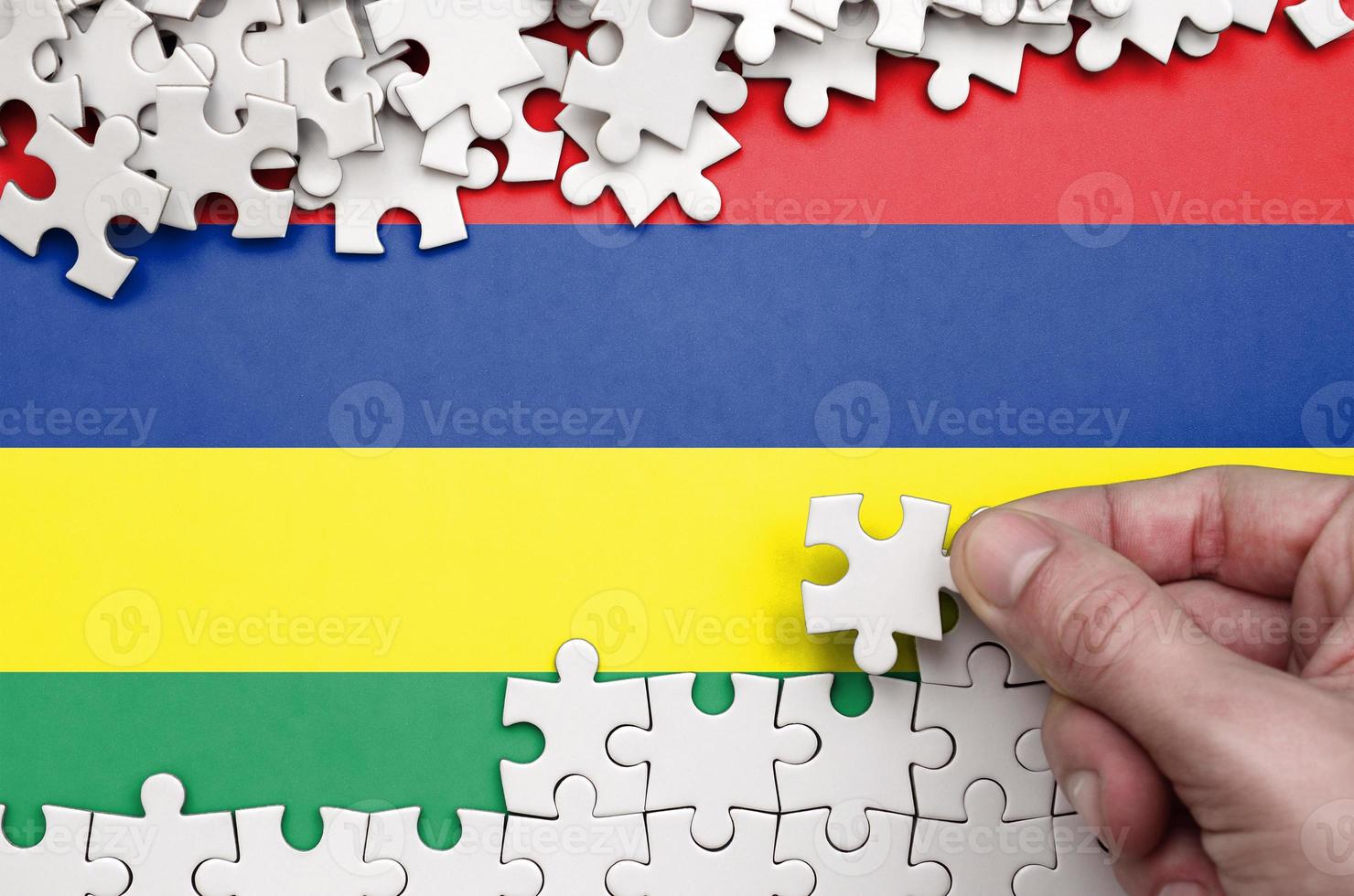 Mauritius flag  is depicted on a table on which the human hand folds a puzzle of white color photo