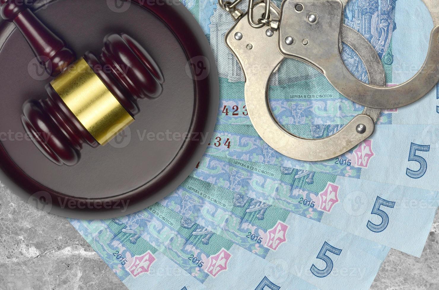 5 Ukrainian hryvnias bills and judge hammer with police handcuffs on court desk. Concept of judicial trial or bribery. Tax avoidance photo