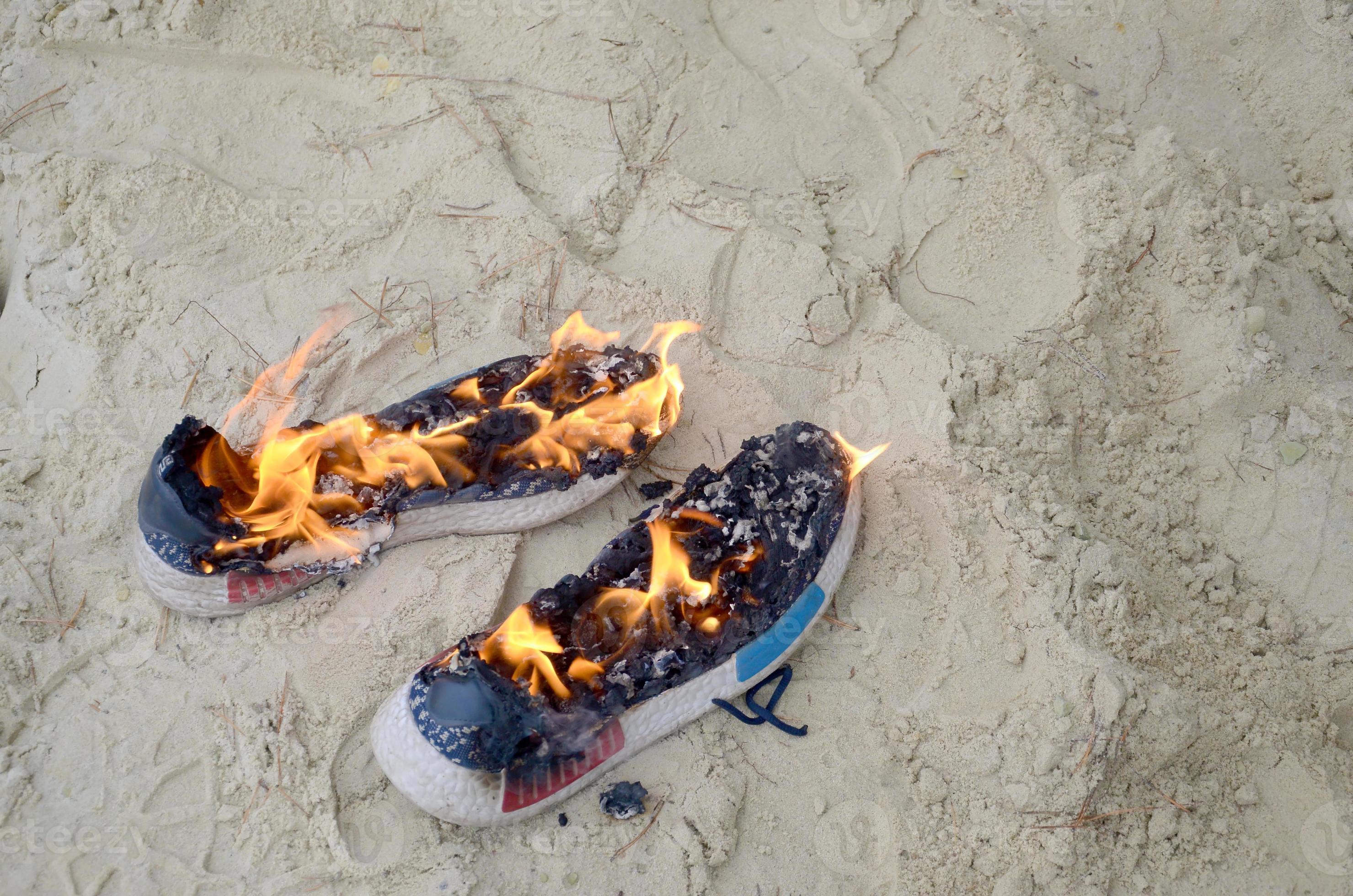 Burning sports sneakers or gym shoes on fire stand on sandy beach coast