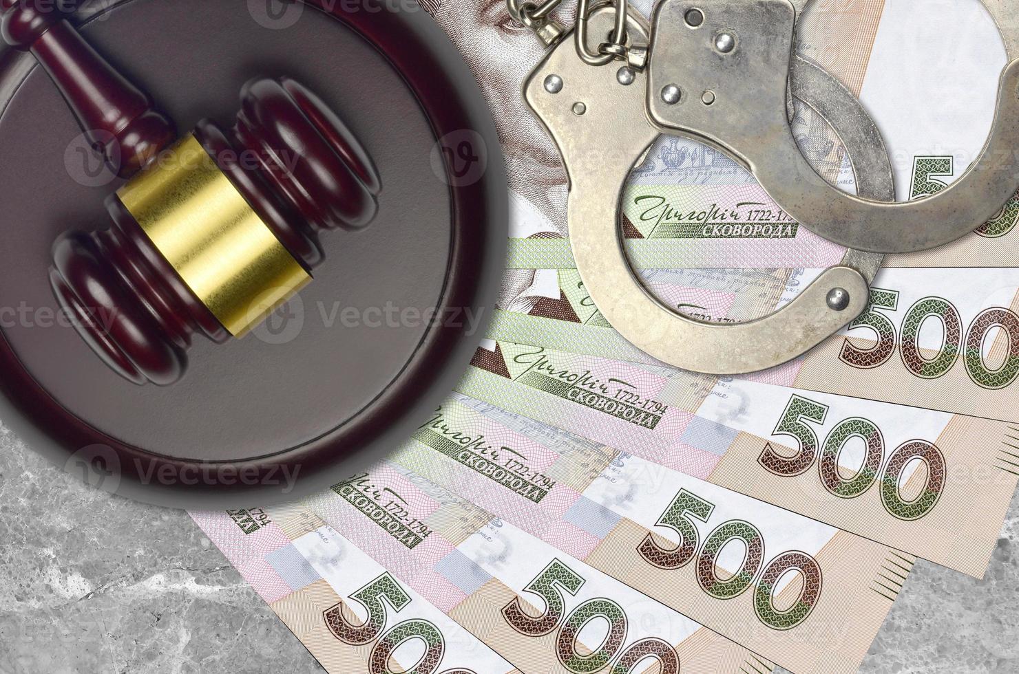 500 Ukrainian hryvnias bills and judge hammer with police handcuffs on court desk. Concept of judicial trial or bribery. Tax avoidance photo