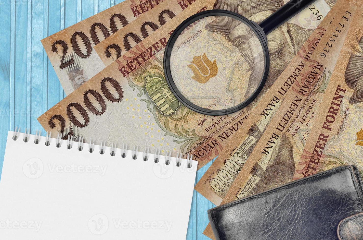 2000 Hungarian forint bills and magnifying glass with black purse and notepad. Concept of counterfeit money. Search for differences in details on money bills to detect fake photo