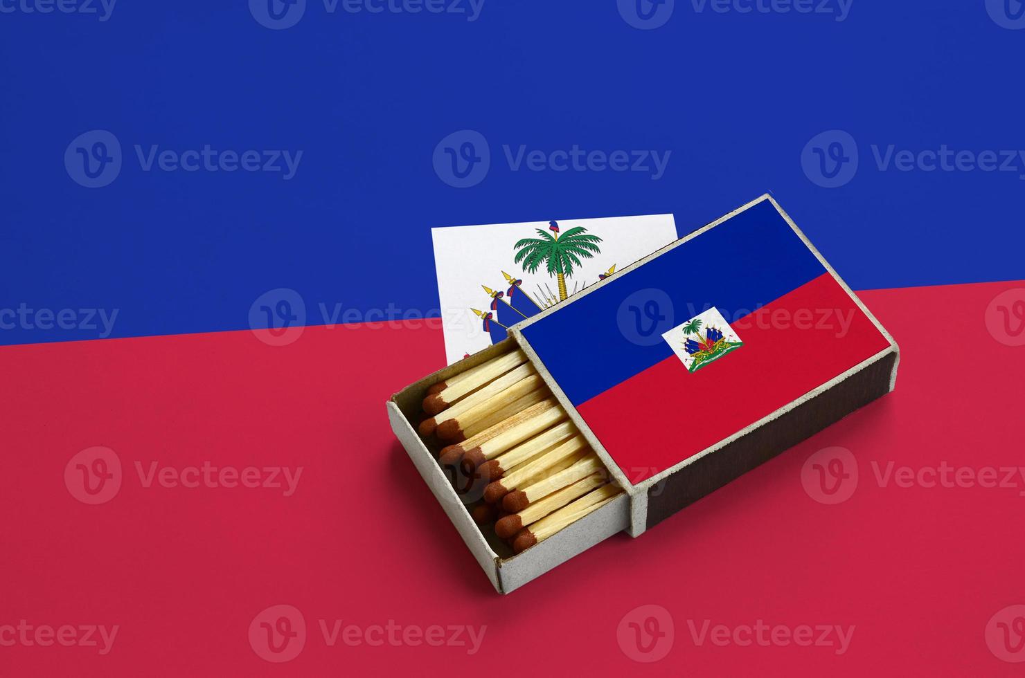 Haiti flag  is shown in an open matchbox, which is filled with matches and lies on a large flag photo