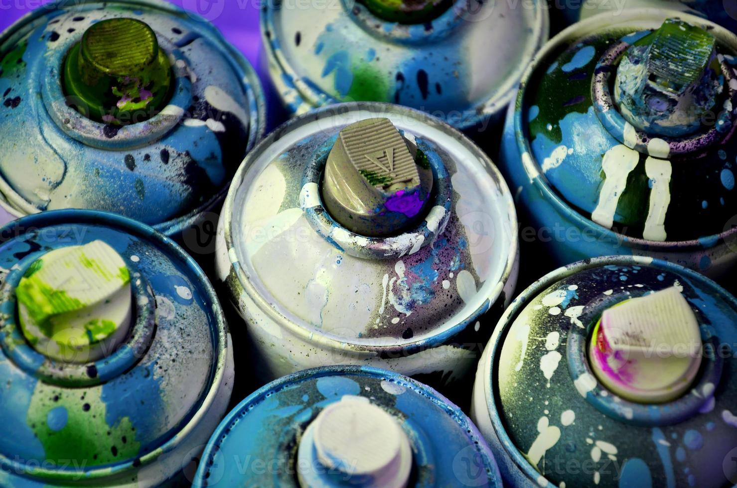 Still life with a large number of used colorful spray cans of aerosol paint lying on the treated wooden surface in the artist's graffiti workshop. Dirty and stained cans for spray art photo