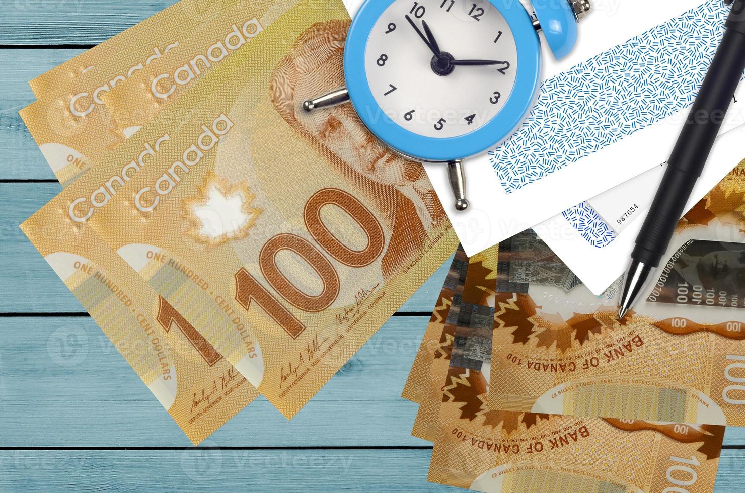 100 Canadian dollars bills and alarm clock with pen and envelopes. Tax season concept, payment deadline for credit or loan. Financial operations using postal service photo