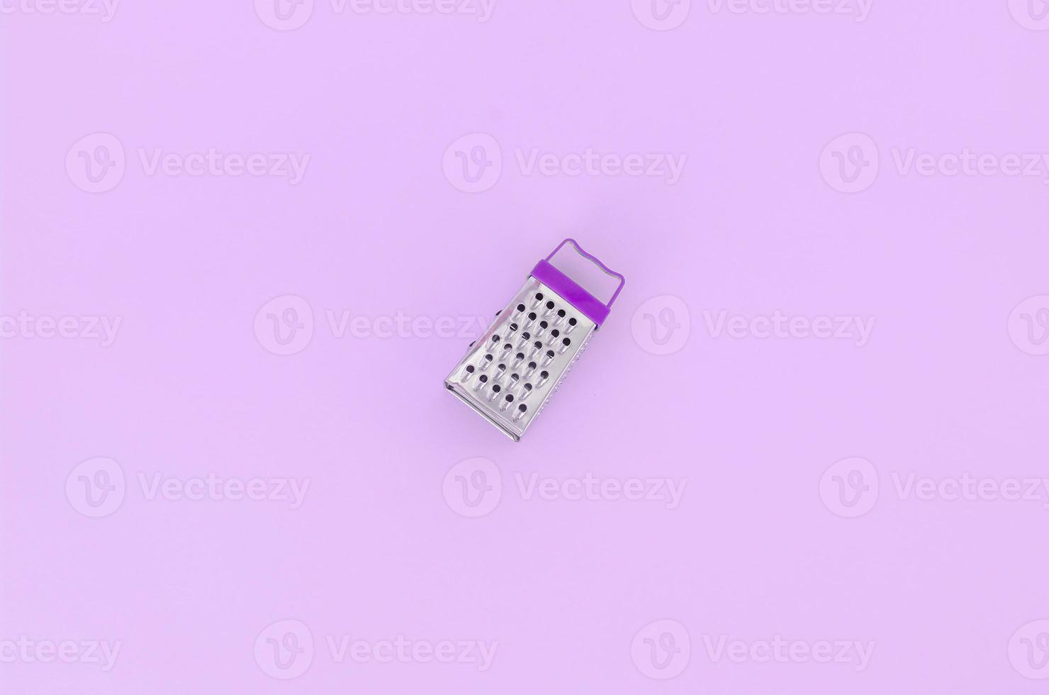 Stainless steel grater lies on a pastel colored paper. Kitchen accessories. Tools for cooking. Flat lay top view photo