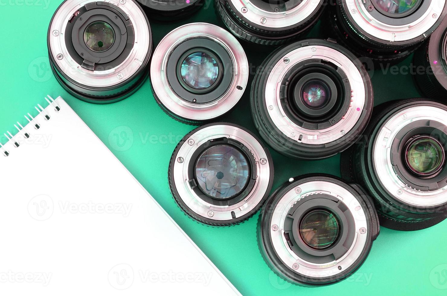 Several photographic lenses and white notebook lie on a bright turquoise background. Copy space photo