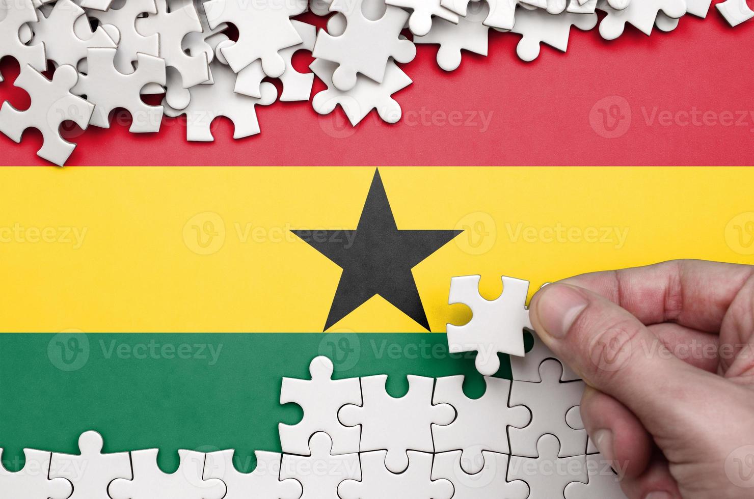 Ghana flag  is depicted on a table on which the human hand folds a puzzle of white color photo