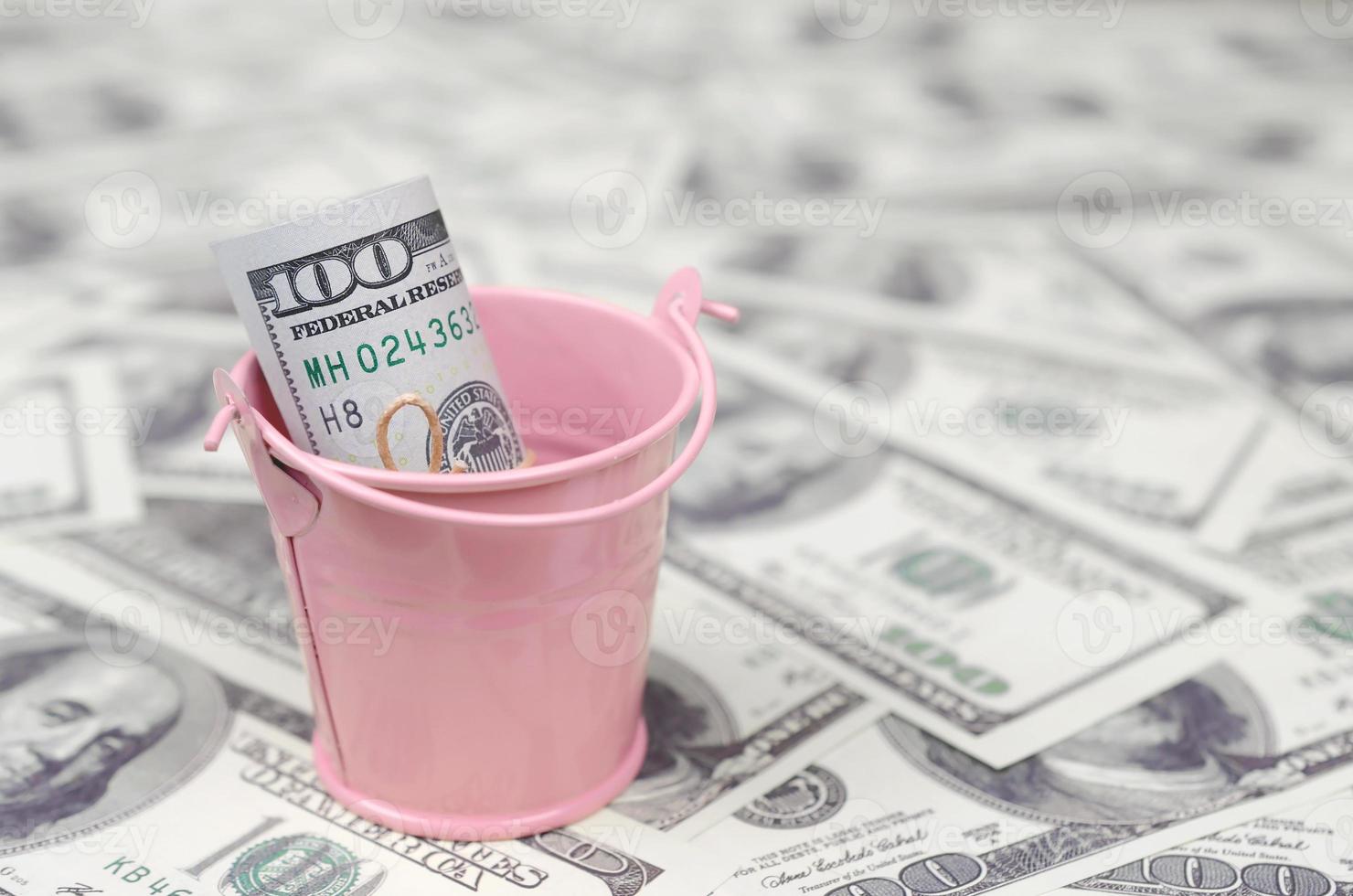 A bundle of US dollars in a metal pink bucket on a set of dollar bills photo