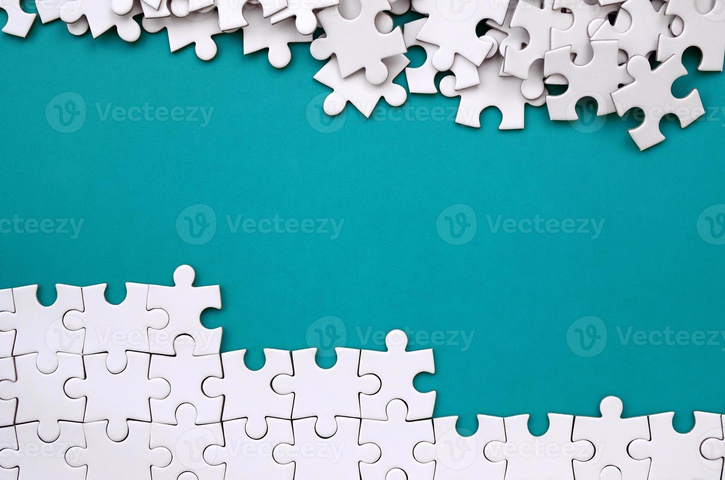 Fragment of a folded white jigsaw puzzle and a pile of uncombed puzzle elements against the background of a blue surface. Texture photo with space for text