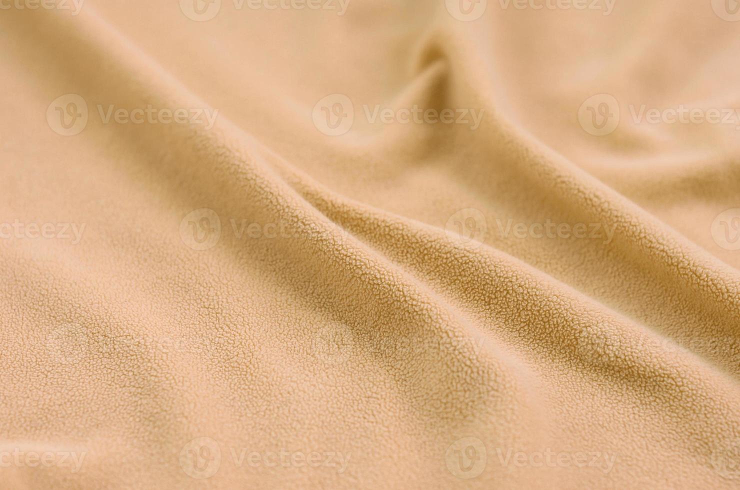 The blanket of furry orange fleece fabric. A background of light orange soft plush fleece material with a lot of relief folds photo