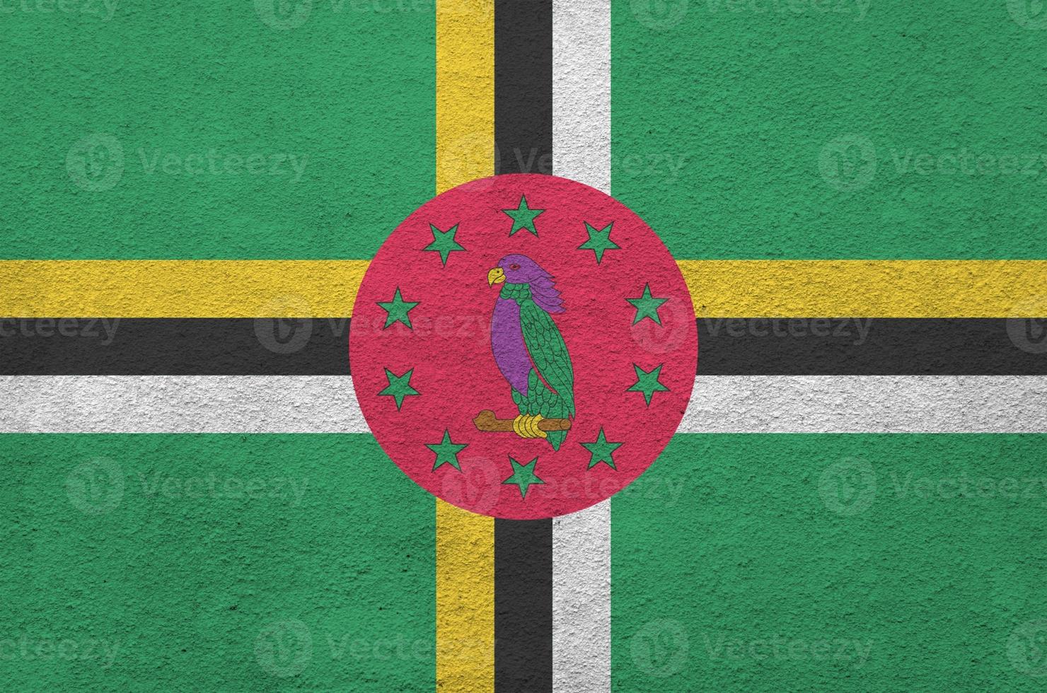 Dominica flag depicted in bright paint colors on old relief plastering wall. Textured banner on rough background photo