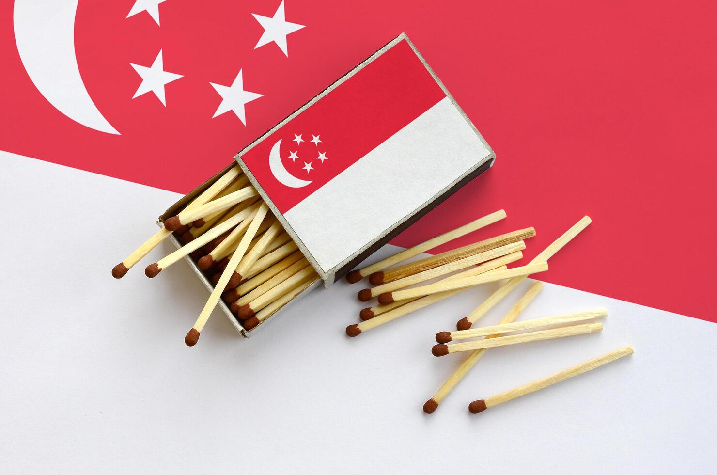 Singapore flag  is shown on an open matchbox, from which several matches fall and lies on a large flag photo