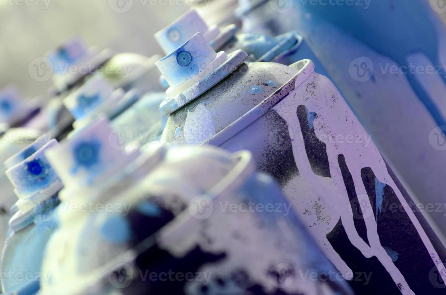 A lot of dirty and used aerosol cans of bright blue paint. Macro photograph with shallow depth of field. Selective focus on the spray nozzle photo