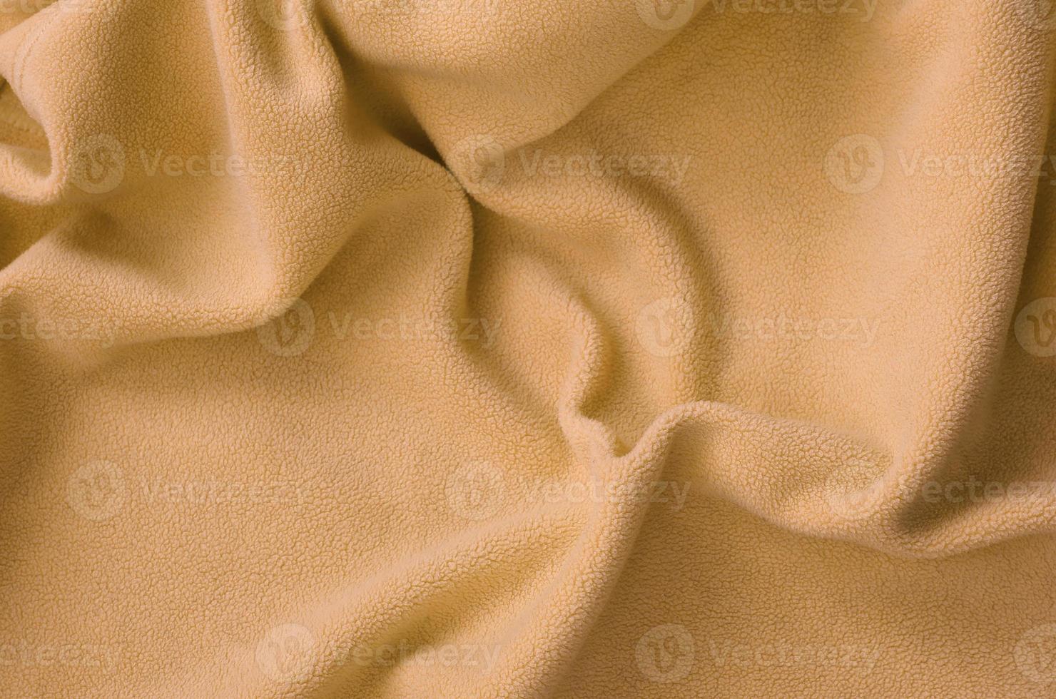 The blanket of furry orange fleece fabric. A background of light orange soft plush fleece material with a lot of relief folds photo