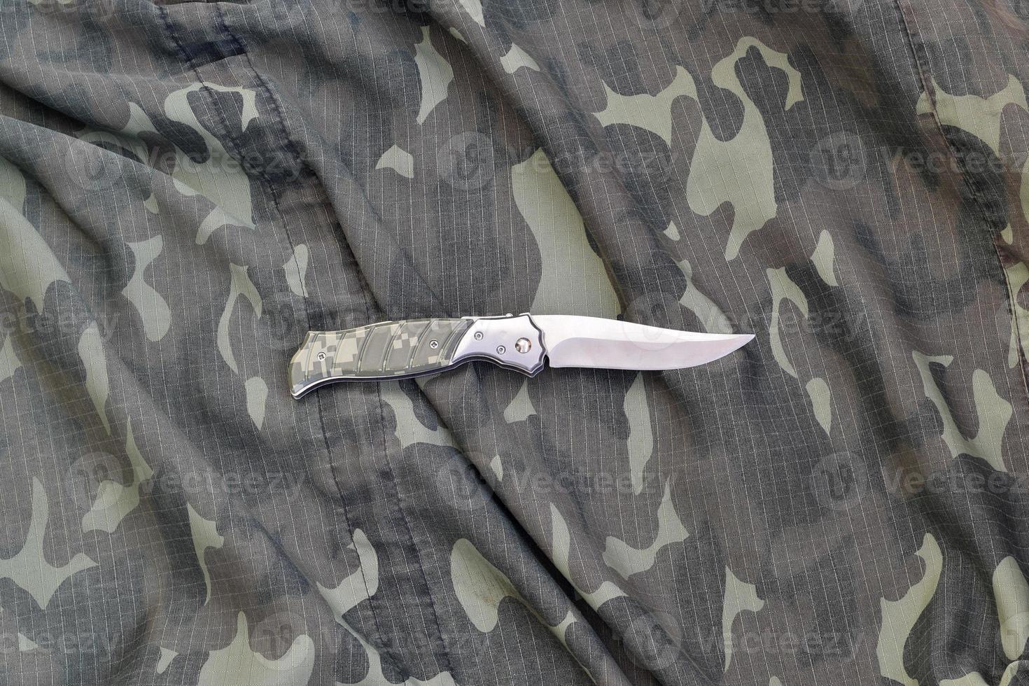 Military knife on army camouflage clothes close up. Background with copy space for military or special service design photo