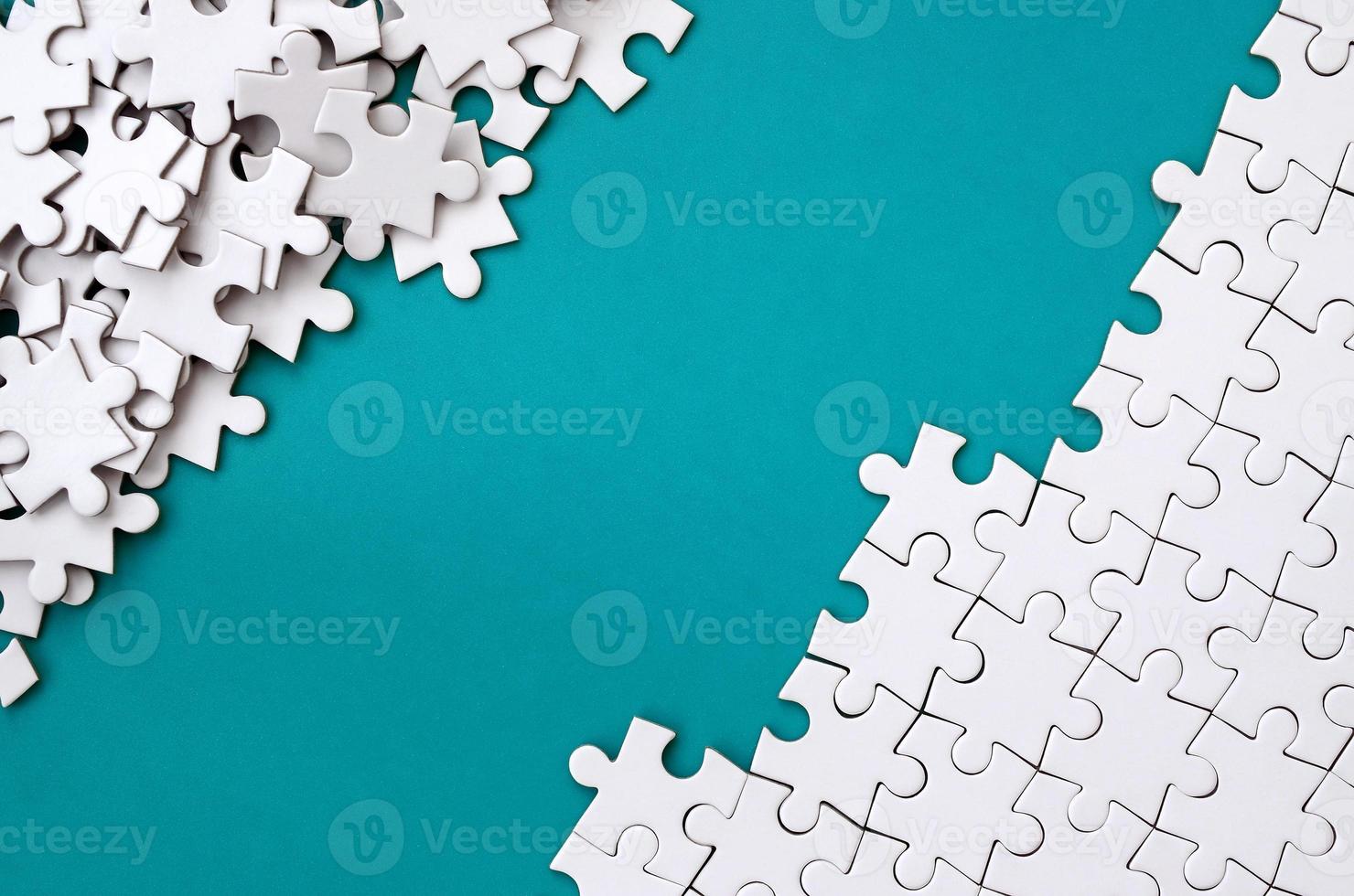 Fragment of a folded white jigsaw puzzle and a pile of uncombed puzzle elements against the background of a blue surface. Texture photo with space for text