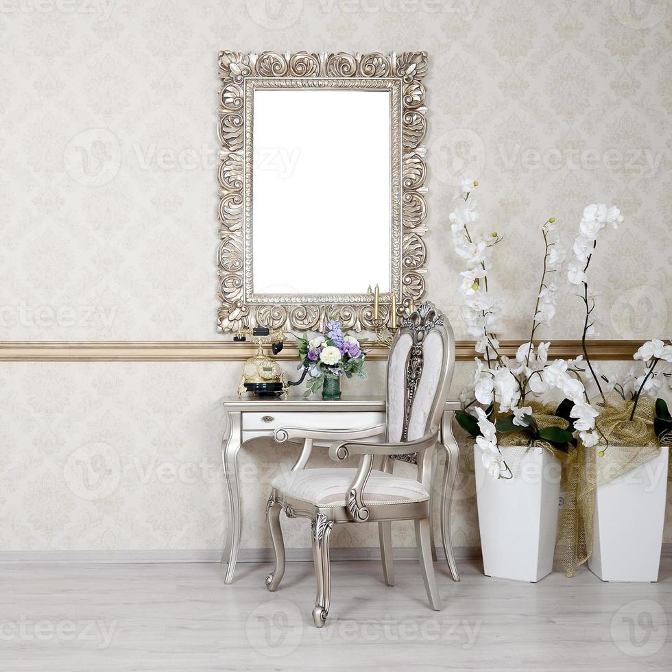 A fragment of a retro interior with a chair and table, on which is a telephone and a vase of flowers. Above the table hangs an empty picture frame for your photo