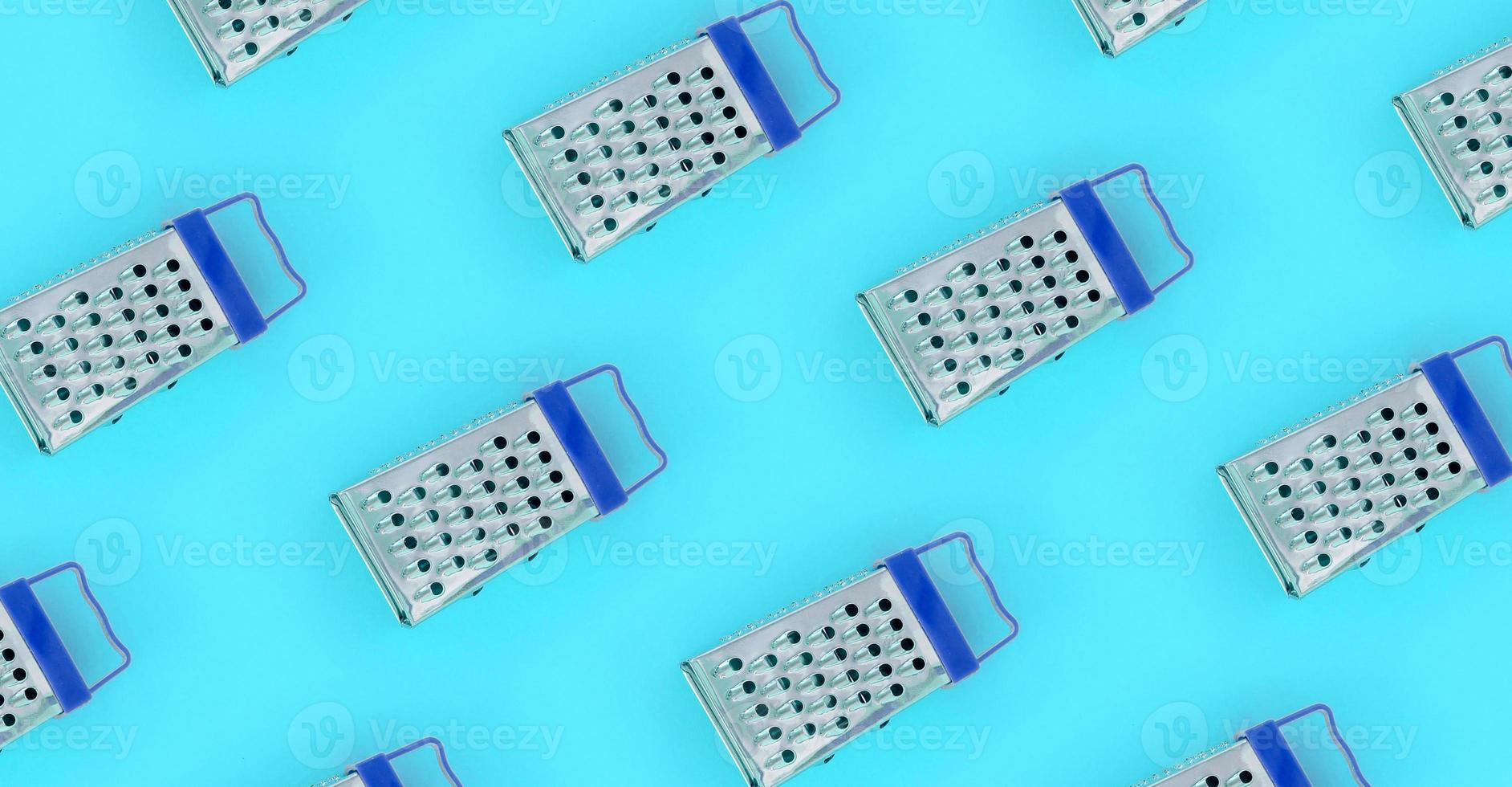 Small stainless steel graters lies on a pastel colored paper. Kitchen accessories. Tools for cooking. Flat lay top view photo