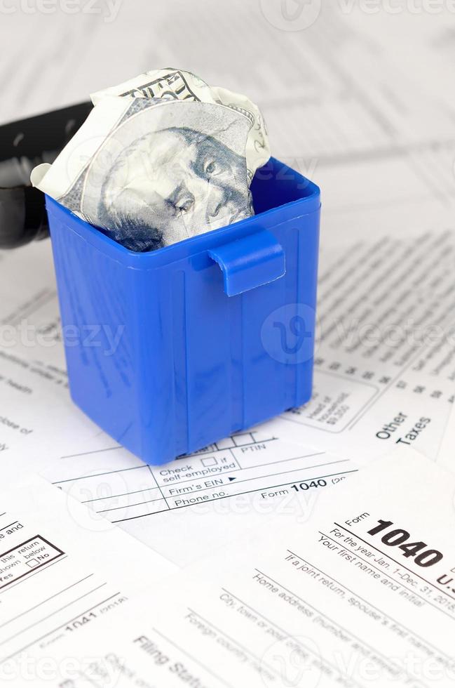 Many american tax blank forms and crumpled hundred dollar bill in trash bin photo