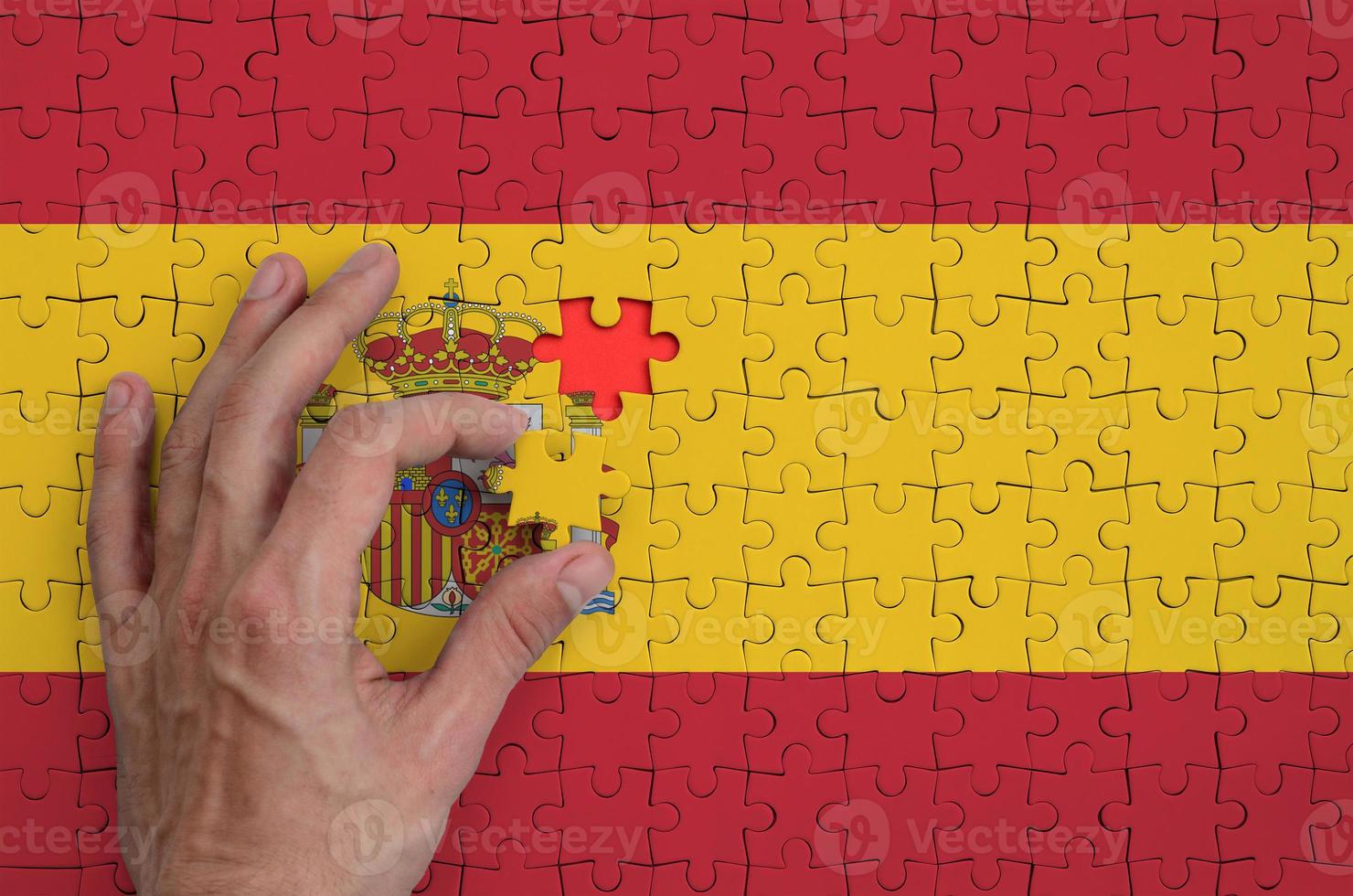 Spain flag  is depicted on a puzzle, which the man's hand completes to fold photo