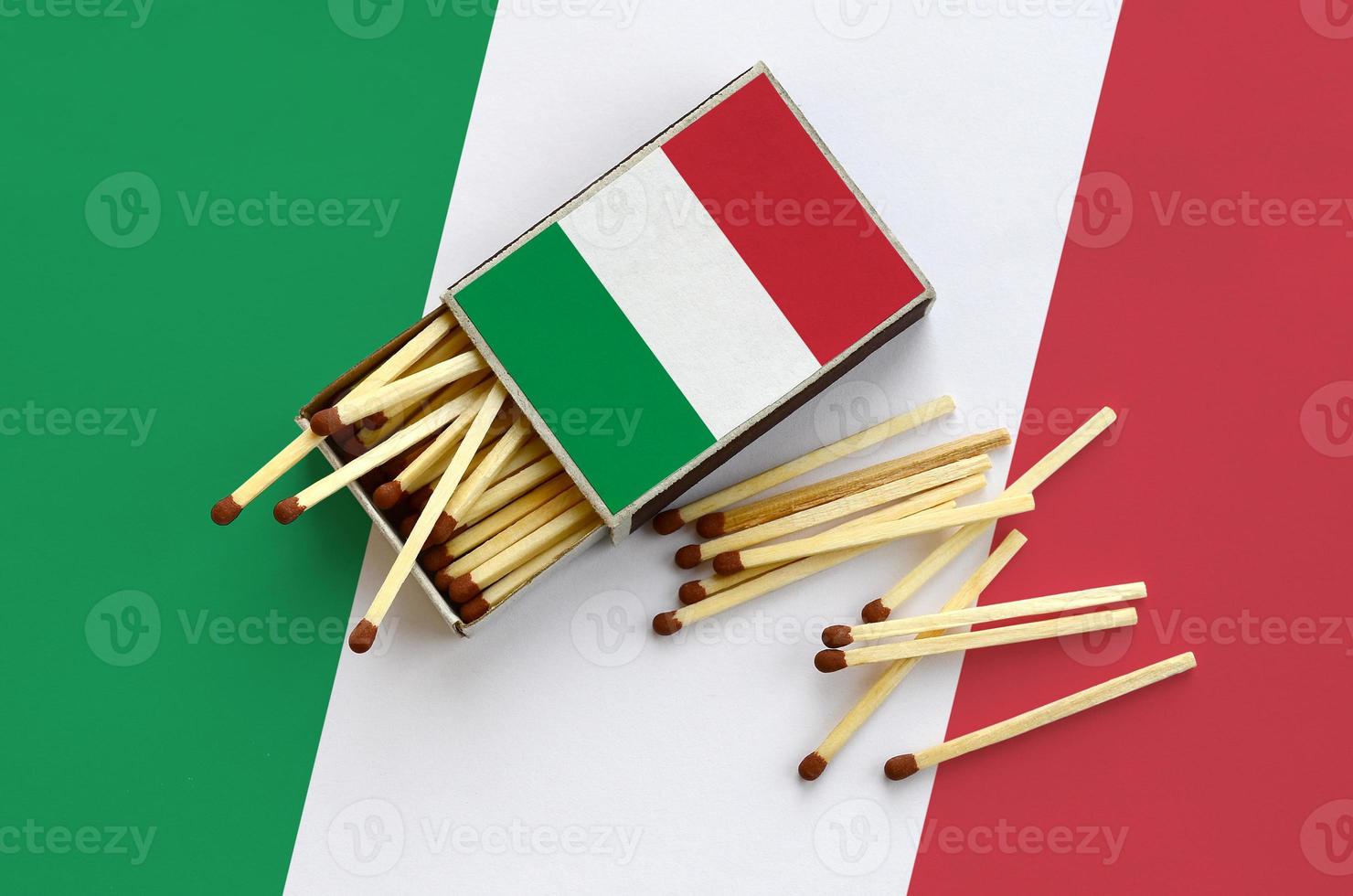 Italy flag  is shown on an open matchbox, from which several matches fall and lies on a large flag photo
