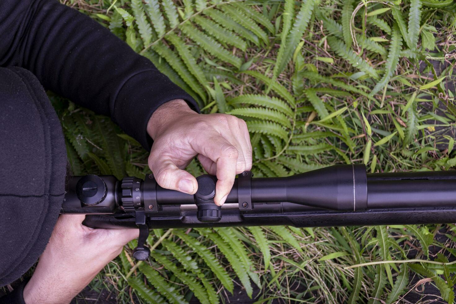 Top view man wearing black hood is shooting rifle looking through scope photo