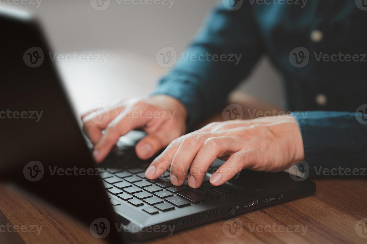 Closeup image of a young man working and typing on laptop computer keyboard on wooden table in cafe. photo