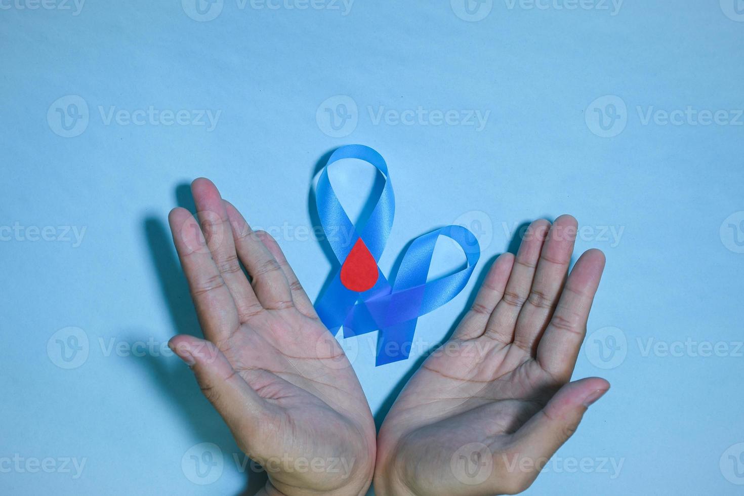 Top View Blue ribbon awareness with red blood drop in man hands isolated on a blue background. 14 november, World diabetes day. Copyspace photo