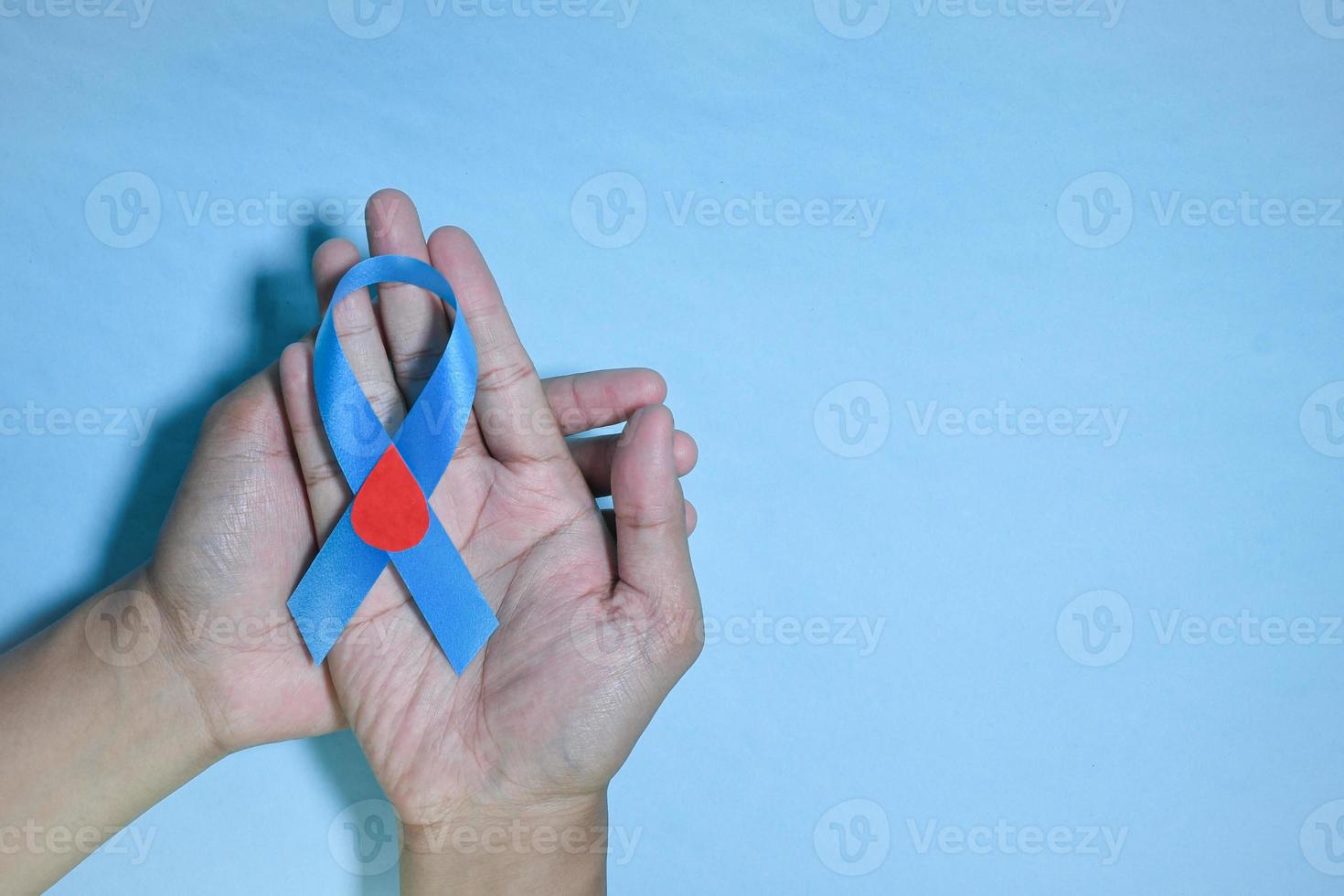 Top View Blue ribbon awareness with red blood drop in man hands isolated on a blue background. 14 november, World diabetes day. Copyspace photo