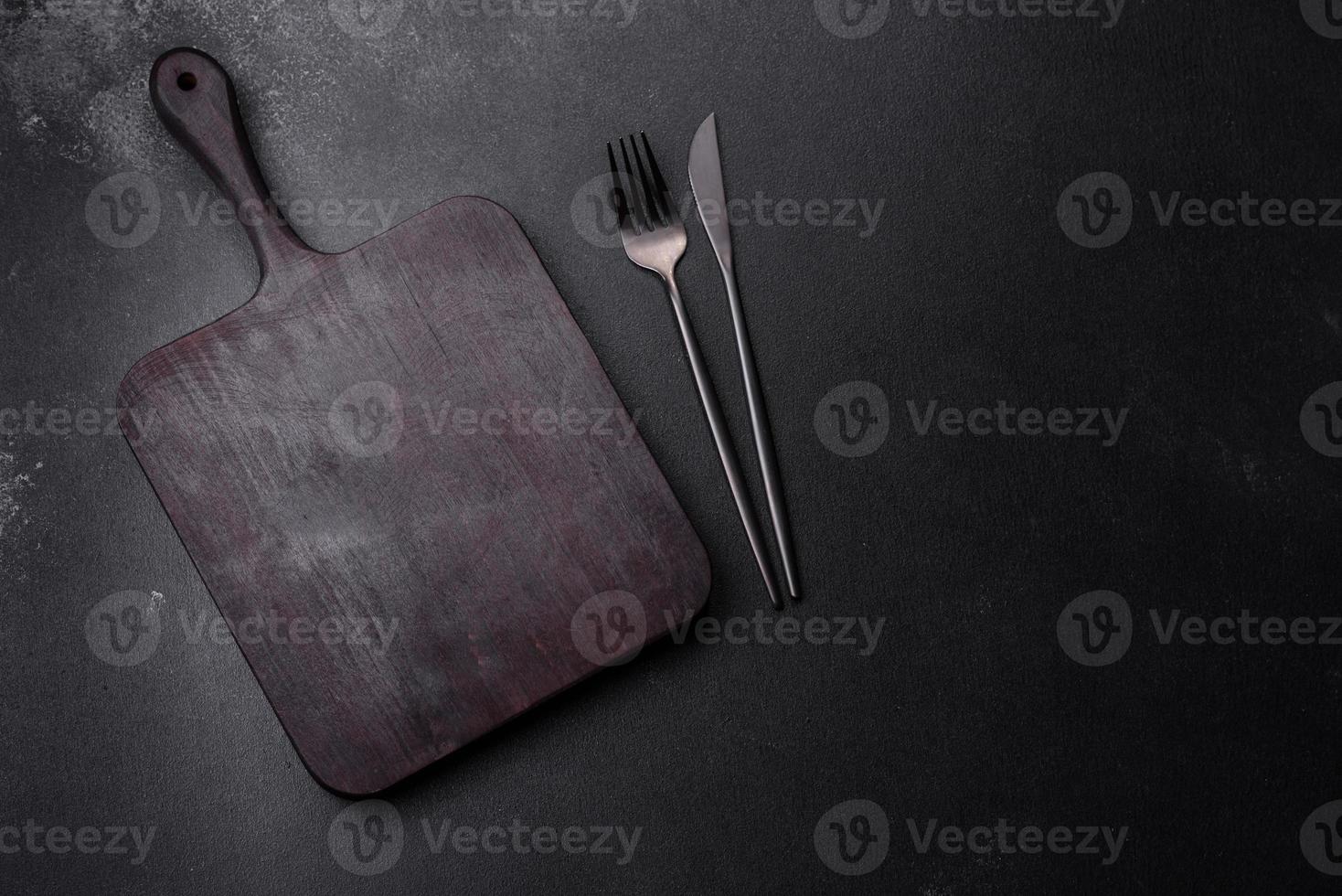 Wooden cutting board with kitchen appliances on a black concrete background photo