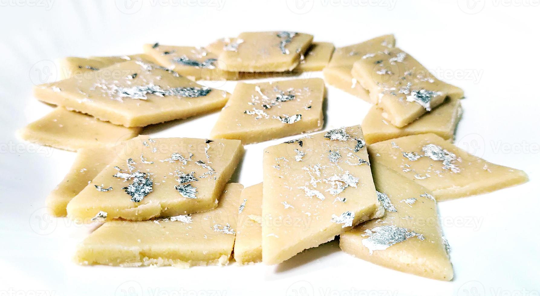 kaju katli es un dulce indio en forma de diamante hecho con azúcar de anacardo y mava, servido en un plato aislado sobre fondo blanco. enfoque selectivo foto