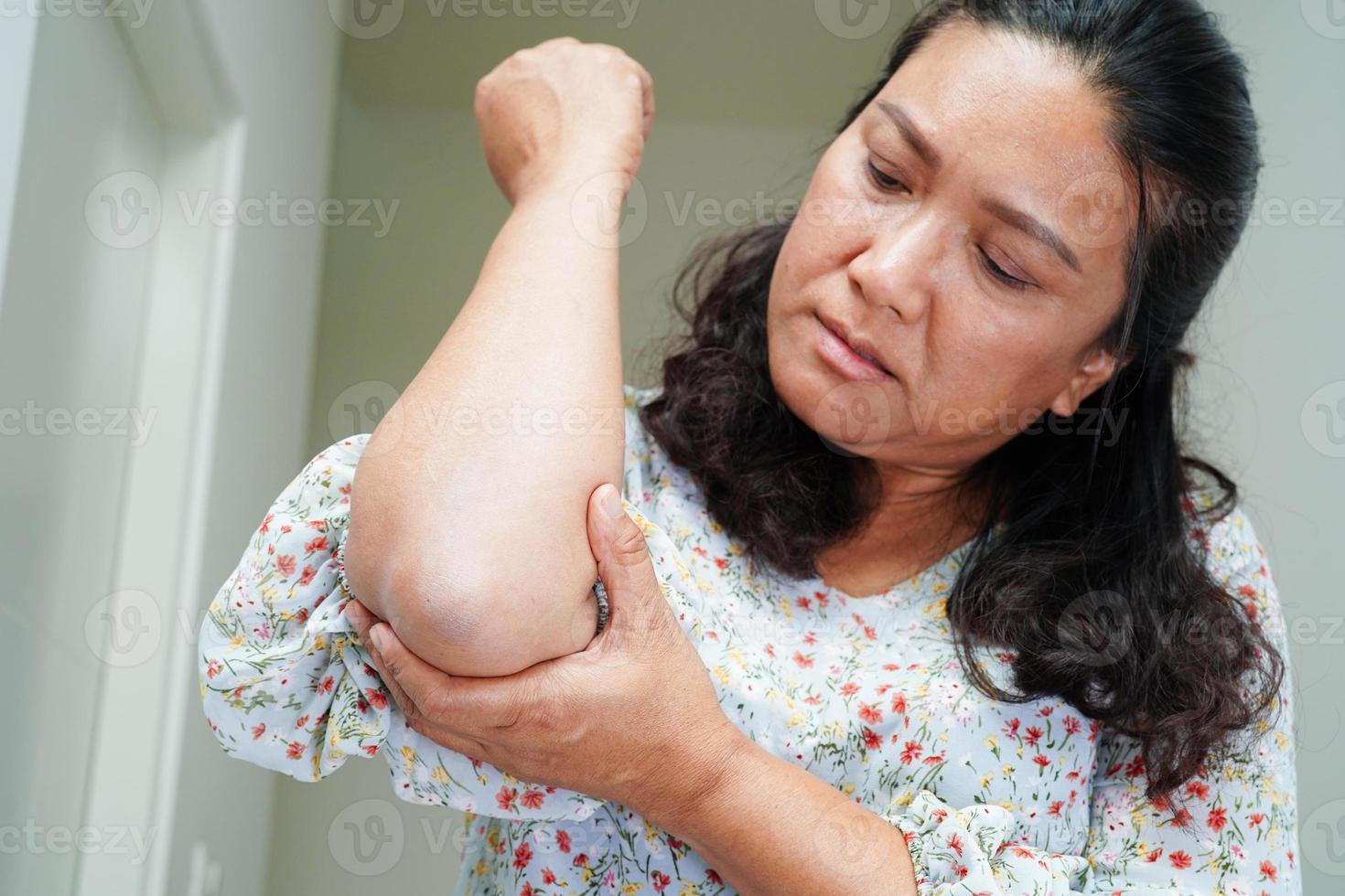 Asian senior woman wearing elastic support elbow brace for reduce pain. photo