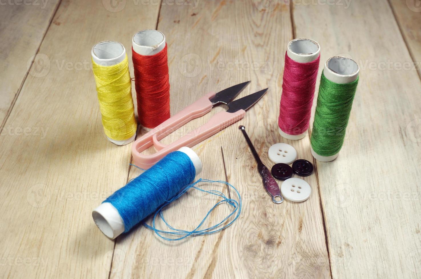 Spools of thread and basic sewing tools including pins, needle, a thimble and a thread cutteron a wooden tabletop. photo