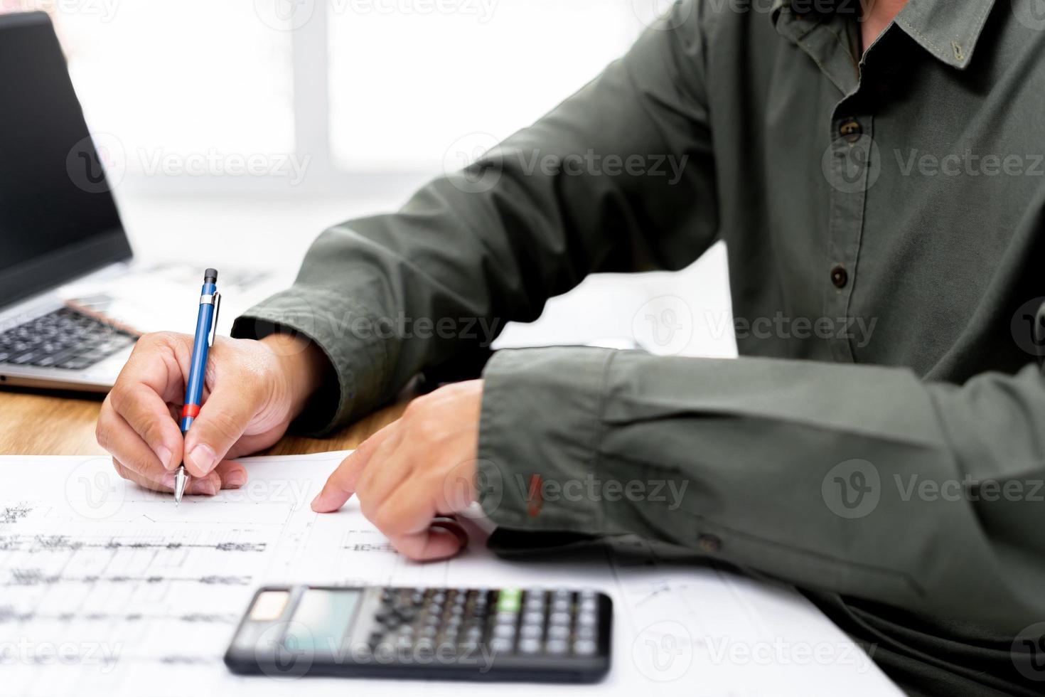 Engineer technician use pencil write in drawing in engineering work  with calculator laptop computer and drawing on table photo