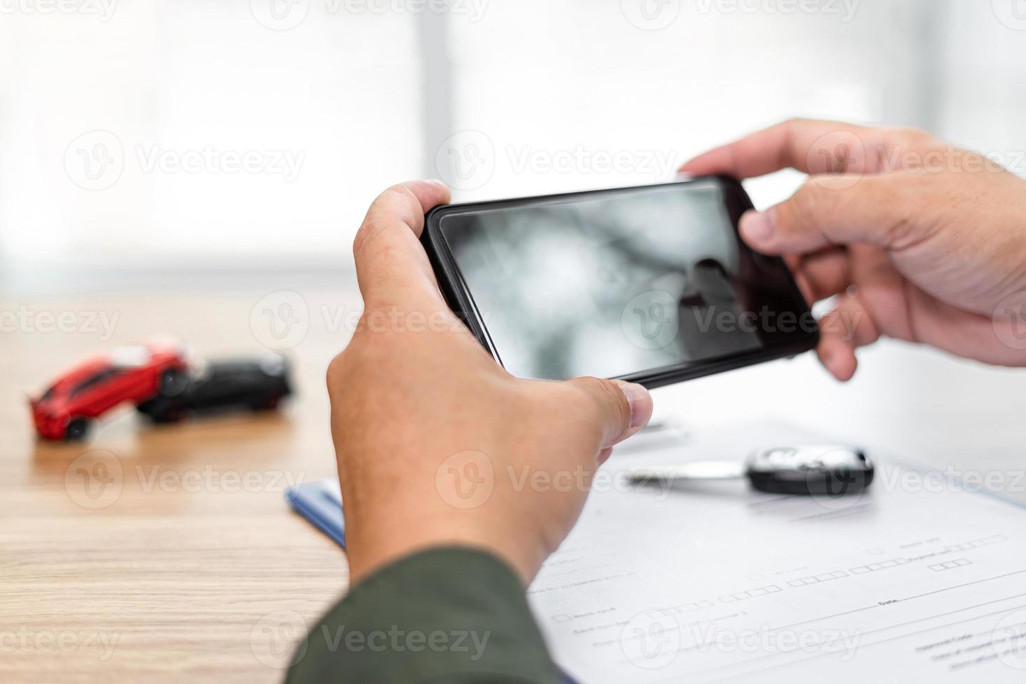 Hand a man hold smartphone take a photo of Car crash accident and document ,car key on table,Safety concept example from Toy car model