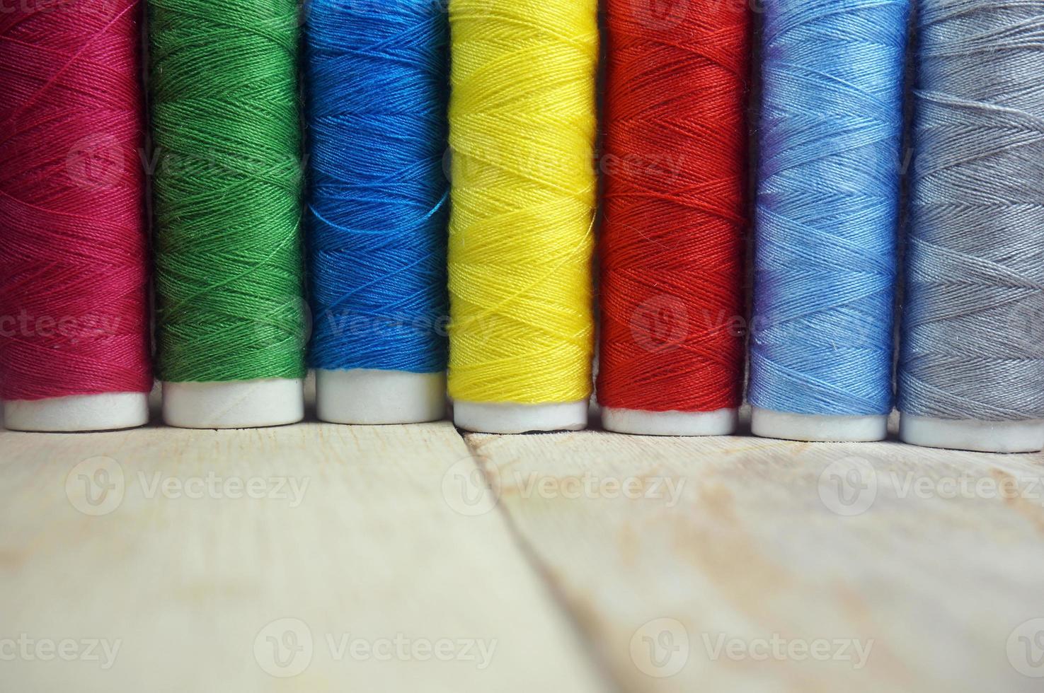 Colorful spools of thread on wooden table photo