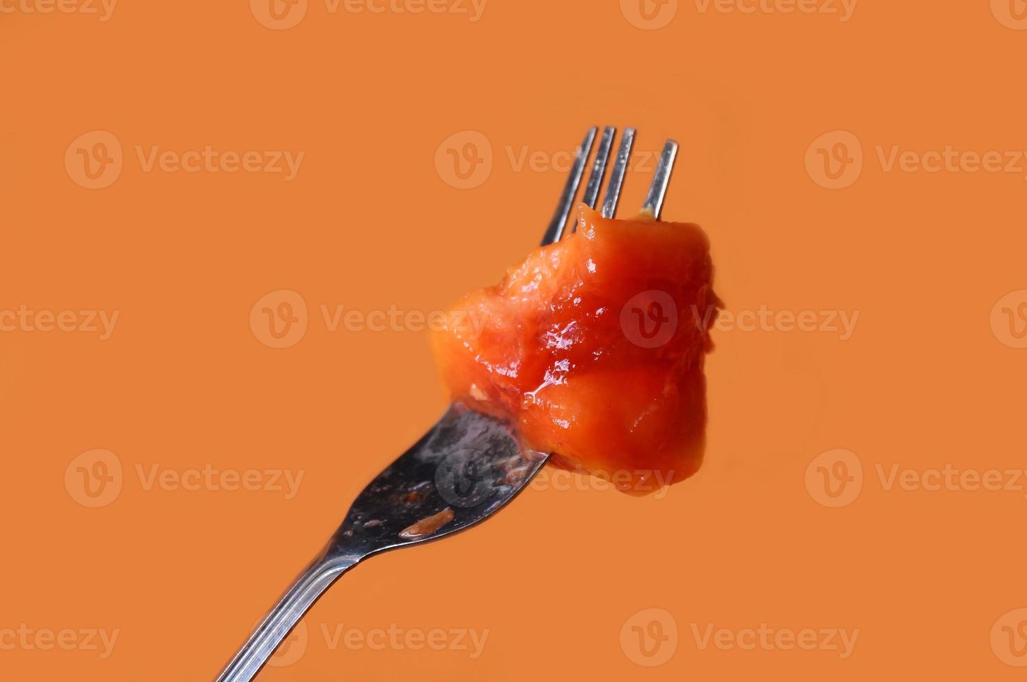 Papaya eating a slice on fork isolated on orange background photo