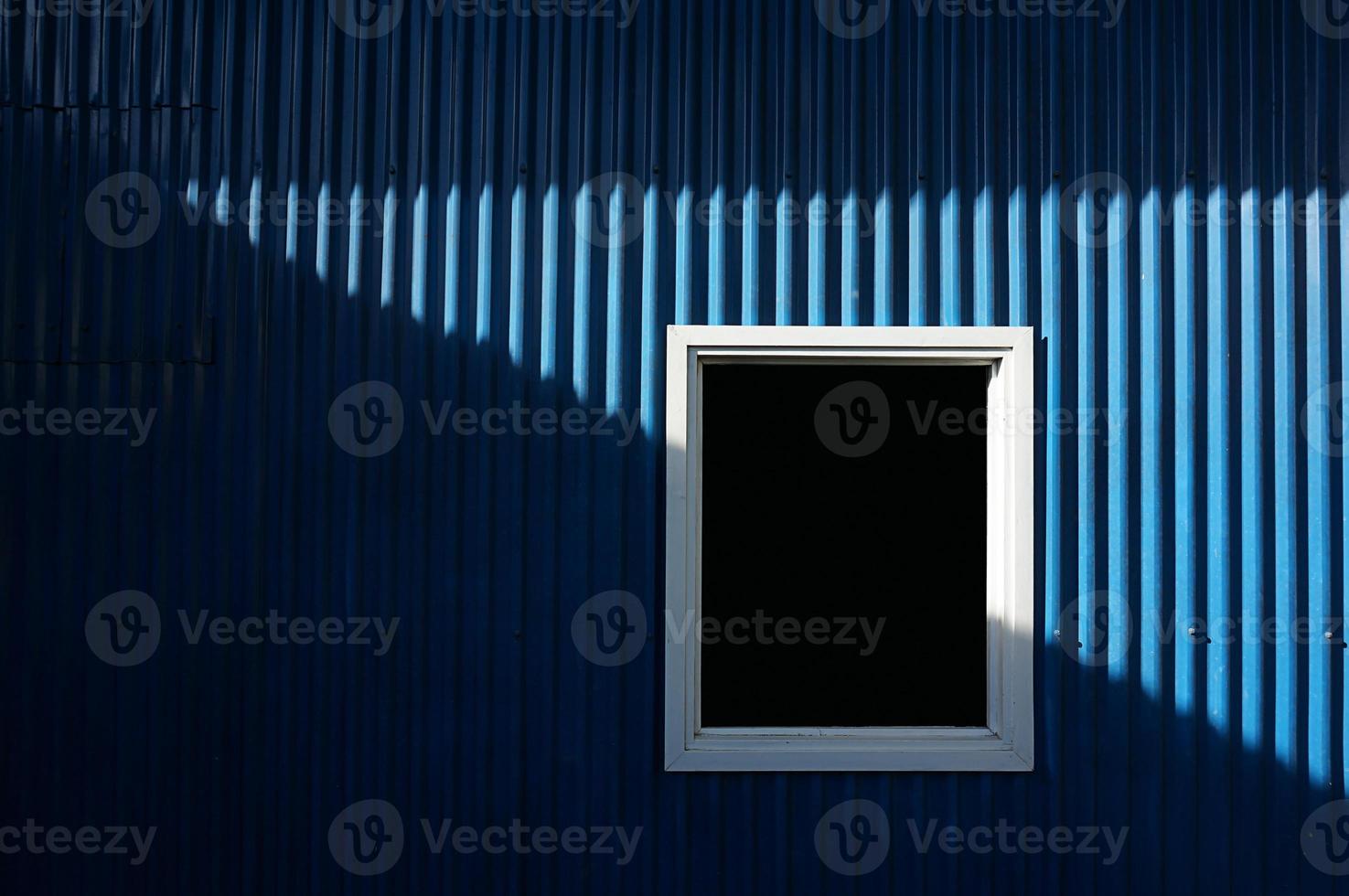 white window on blue metal wall with sunlight and shadow. photo