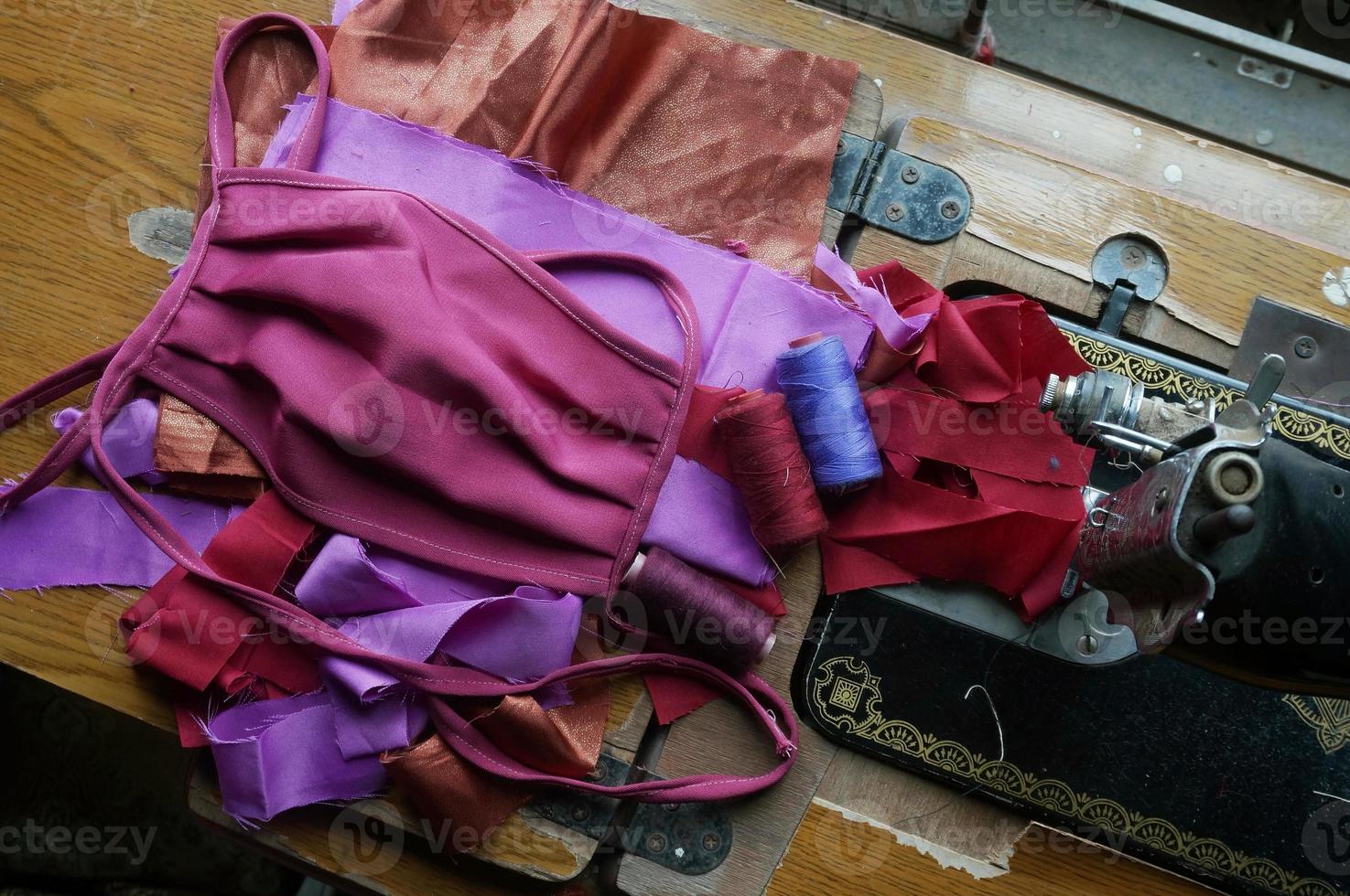 Homemade protective mask and pieces of cloth on wooden of manual sewing machine. Selective Focus. photo