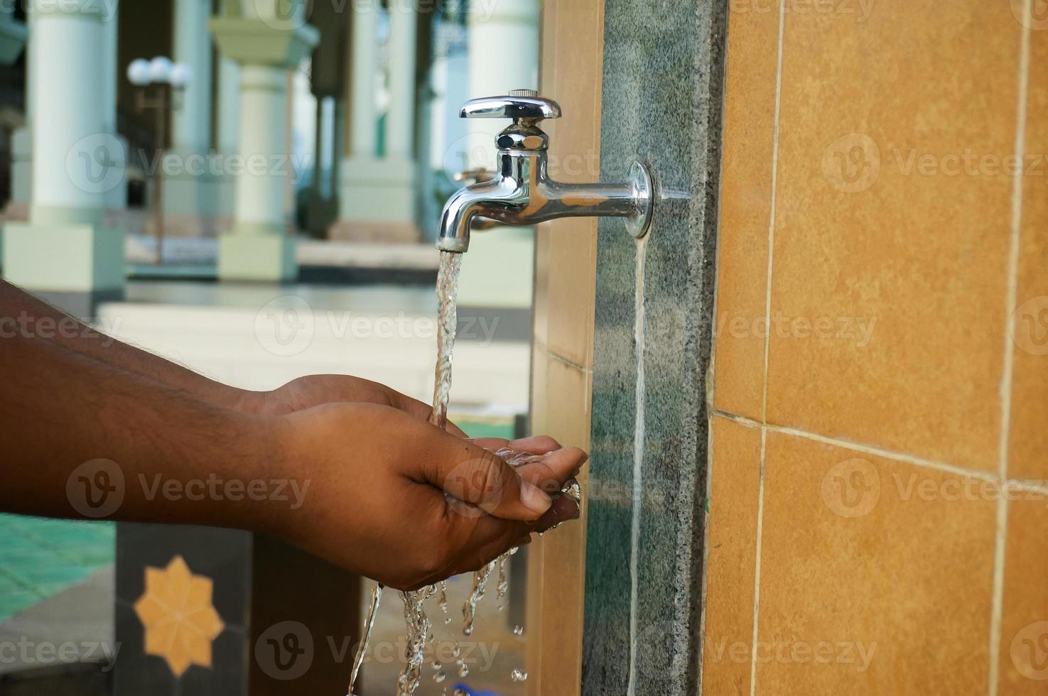 A moslem man take ablution, known as wudhu, as one of ritual purification to pray, washing hand.  Outside mosque. photo