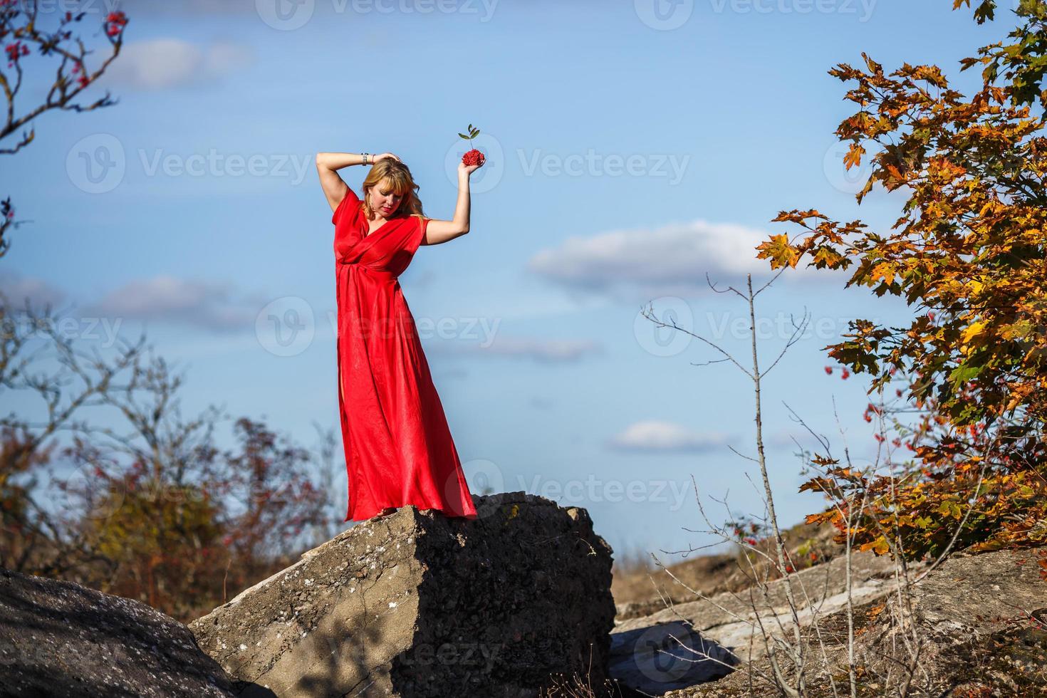 girl in red dress on rock or concrete ruined structure with rowan on autumn background photo