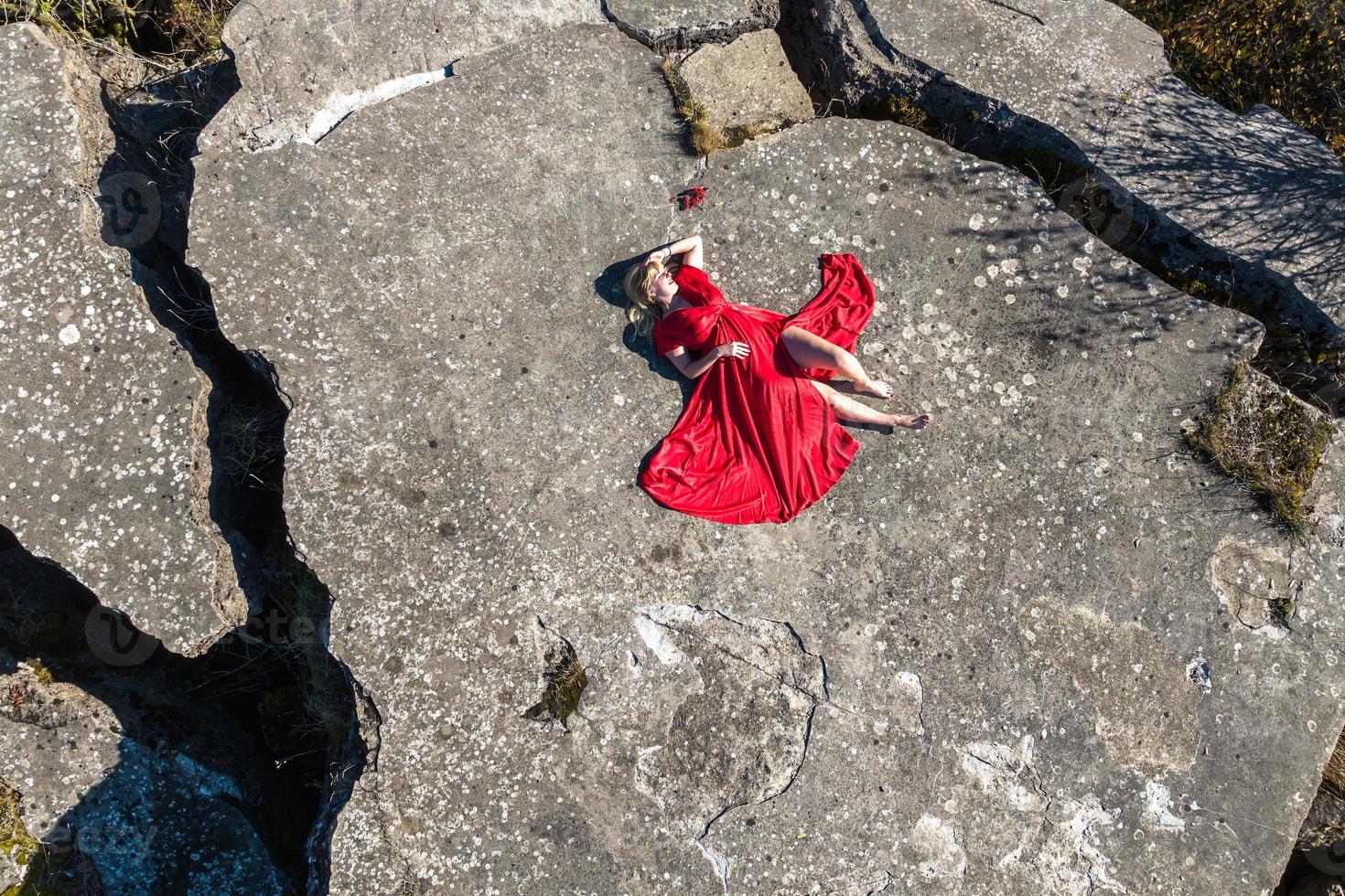 vista aérea de una chica con vestido rojo sobre roca o estructura en ruinas de hormigón foto