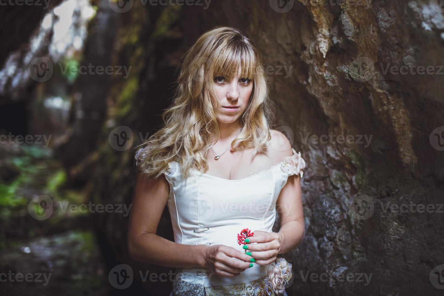 hermosa chica rubia con un vestido blanco con un corsé en una cueva profunda y oscura foto